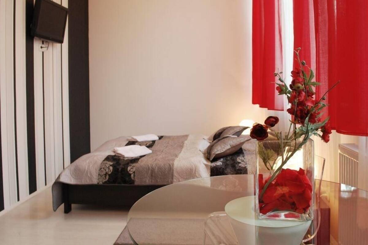 Une chambre à coucher avec un lit, une table de chevet, un vase de fleurs et un téléviseur fixé au mur.