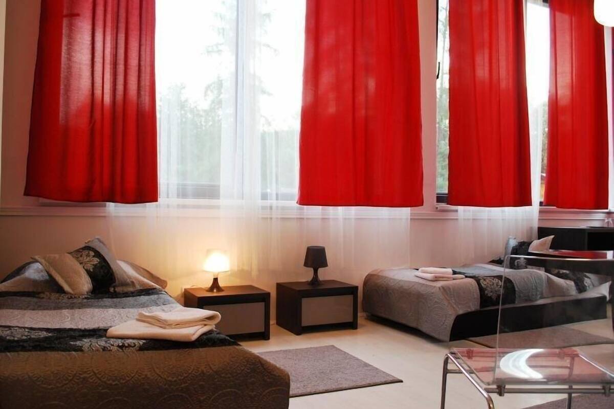 Une chambre moderne avec un lit, des tables de chevet, une table basse en verre et des rideaux rouges.