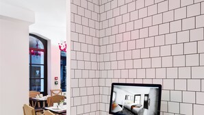 Una habitación de hotel moderna con pared de ladrillo blanco, sillas de madera, un escritorio con computadora y una ventana con vista a la ciudad.