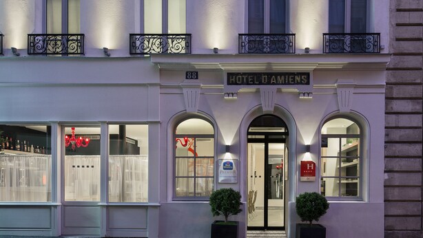 Fachada de hotel de estilo arquitectónico clásico, con varios balcones con barandillas de hierro forjado, ventanas grandes y una entrada destacada con un letrero que dice “HOTEL D'AMIENS”.