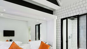 Una habitación de hotel moderna con una cama grande, ropa de cama naranja, un televisor de pantalla plana y un amplio ventanal con vistas a la ciudad.