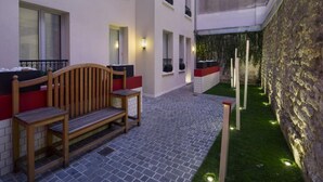 Un patio con un banco de madera, una mesa pequeña y una pared con luces verticales.