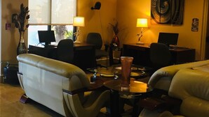 A hotel lobby with leather sofas, two desks with computers, a large window, and a painting on the wall. - Marble Waters Hotel & Suites, Trademark by Wyndham (Jacksonville)