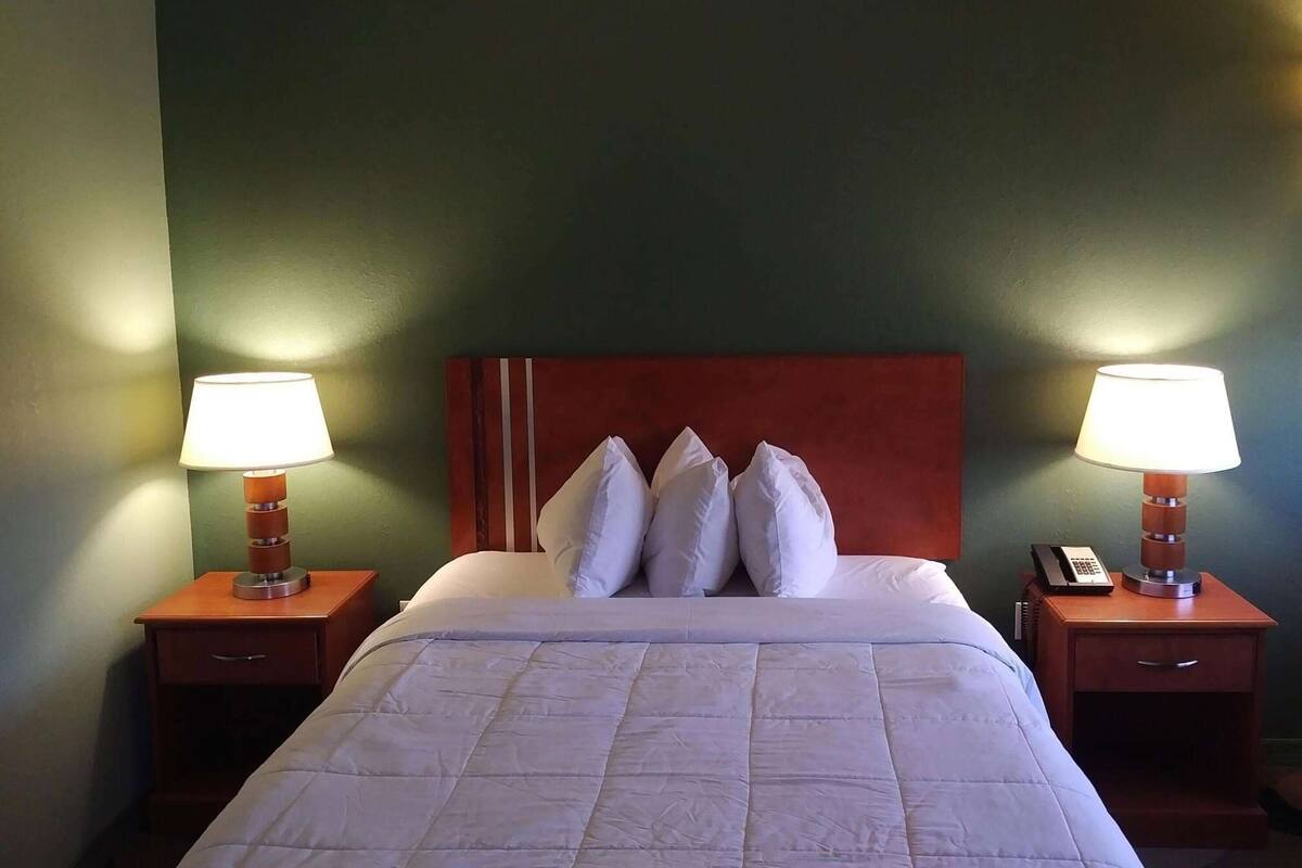 A hotel room with a bed, two bedside tables with lamps, a telephone, and a red headboard.