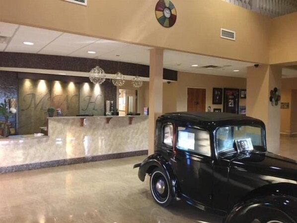 A vintage car in a hotel lobby with a reception desk and chandeliers.