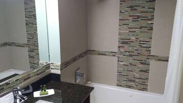 A bathroom with a granite countertop, a white sink, a mirror, a shower, and a mosaic tile wall.
