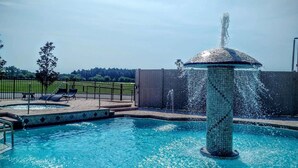 A swimming pool with a central fountain, surrounded by a fenced area with lounge chairs and a tree. - Marble Waters Hotel & Suites, Trademark by Wyndham (Jacksonville)