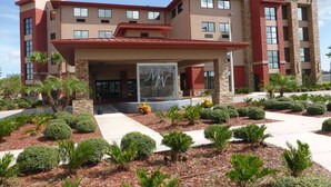 A hotel with a modern design, featuring a prominent entrance with a glass facade and a red roof. - Marble Waters Hotel & Suites, Trademark by Wyndham (Jacksonville)