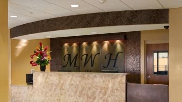 A reception desk with a marble top and a sign displaying 'MWH'. - Marble Waters Hotel & Suites, Trademark by Wyndham (Jacksonville)