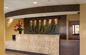 A reception desk with a marble top and a sign displaying 'MWH'. - Marble Waters Hotel & Suites, Trademark by Wyndham (Jacksonville)