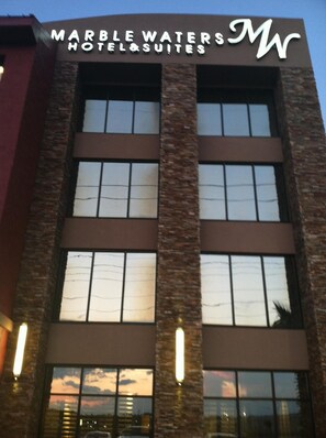 Marble Waters Hotel & Suites features a modern architectural design with large windows and a prominent sign.