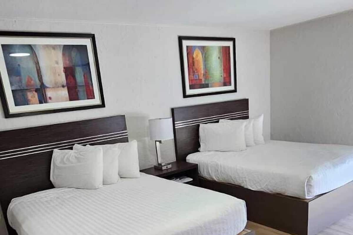 Quarto de hotel com duas camas, uma escrivaninha e uma cadeira.
