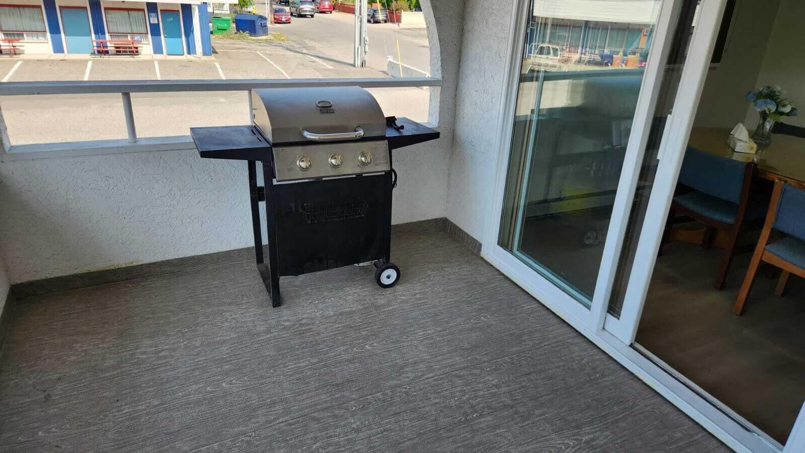 Un pequeño balcón con una parrilla portátil, una puerta corrediza de vidrio y vista a un estacionamiento.