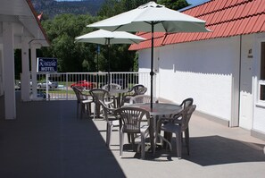 Un patio de motel con mobiliario exterior y sombrillas, un edificio blanco con techo rojo y un cartel que dice Riverside Motel.