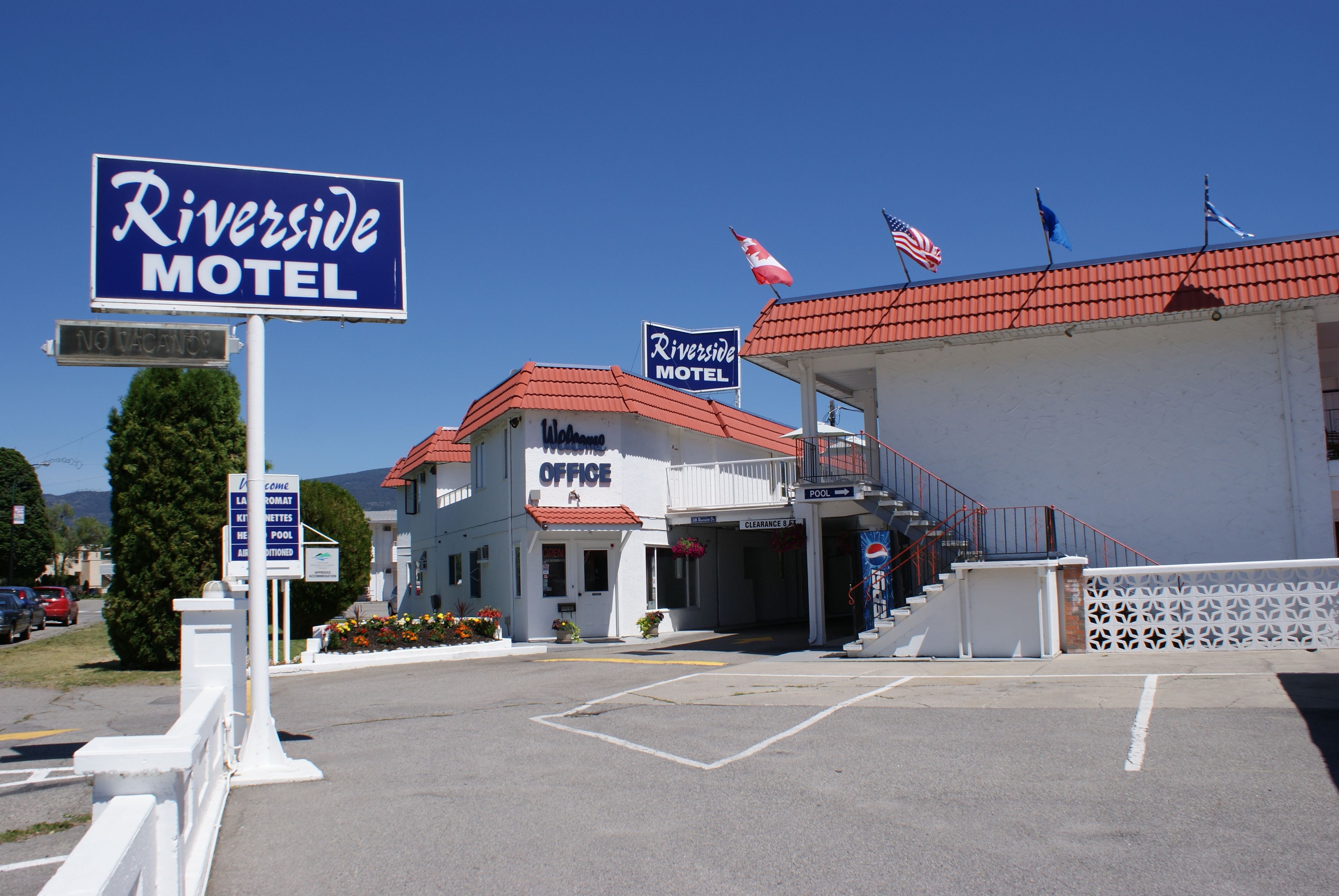Un motel a orillas del río, con techo rojo, una oficina visible y un estacionamiento.
