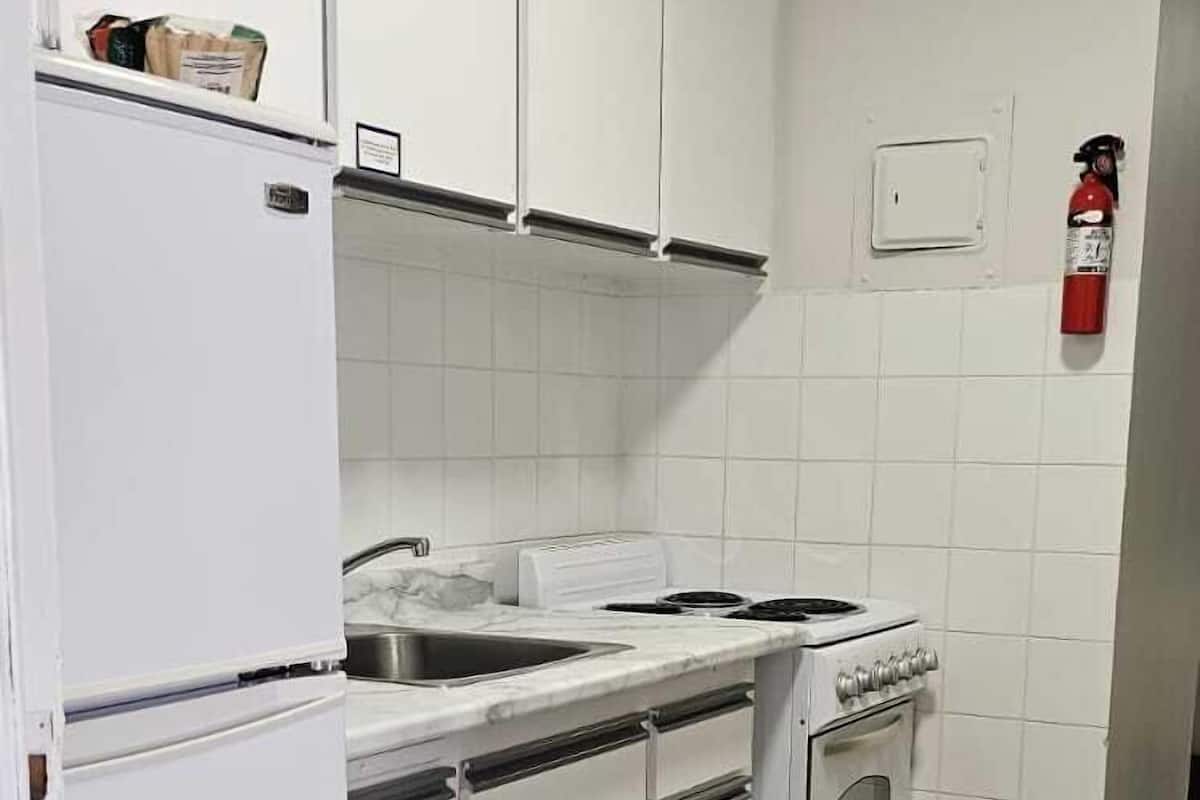 Cozinha compacta com armários brancos, forno embutido, pia e geladeira.
