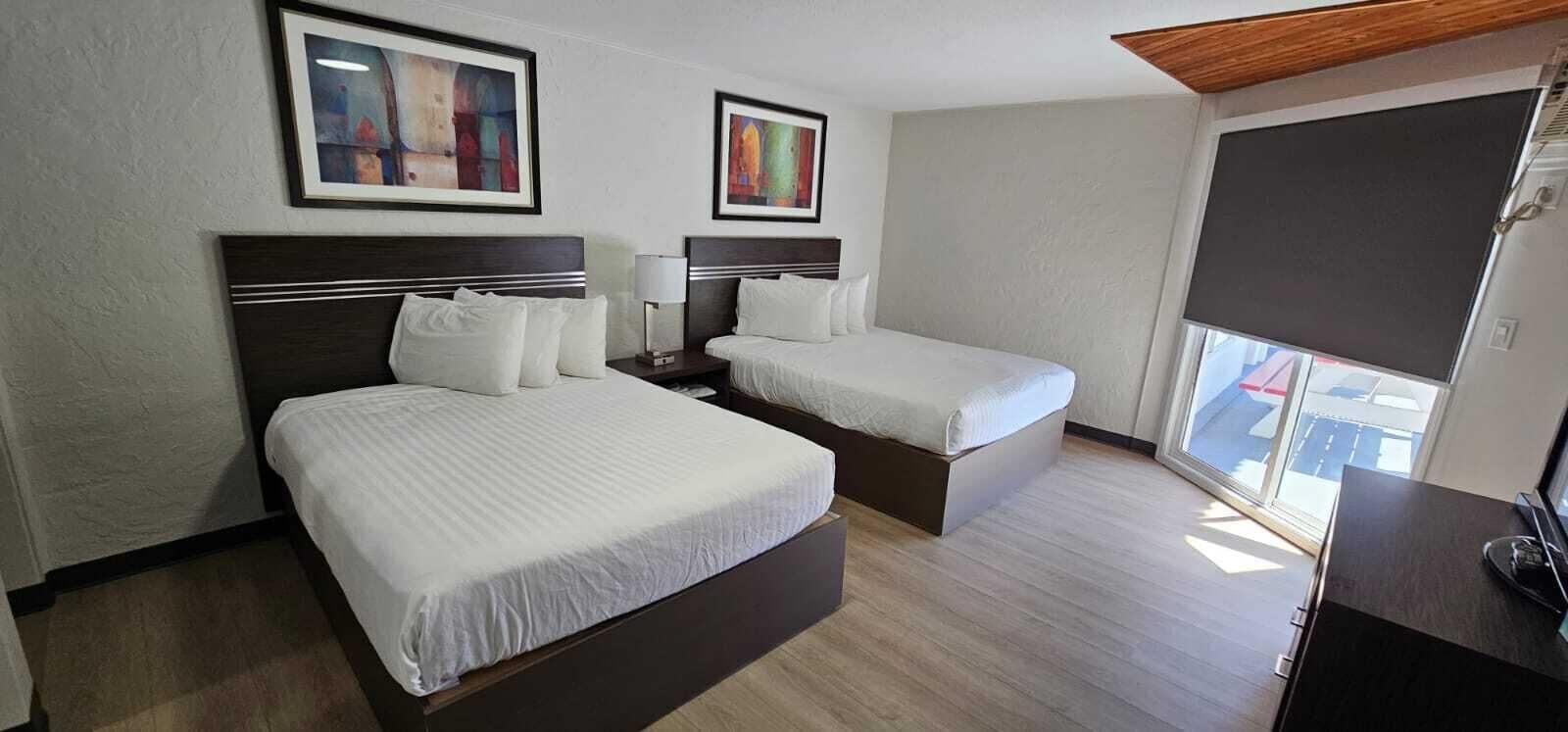 Ett hotellrum med två sängar, ett skrivbord, en TV och konstverk på väggarna.