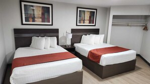 A hotel room with two beds, a nightstand, a lamp, and two framed artworks on the wall. - Riverside Motel (Penticton)