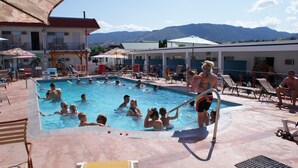 A swimming pool area with multiple pools, lounge chairs, and umbrellas. - Riverside Motel (Penticton)