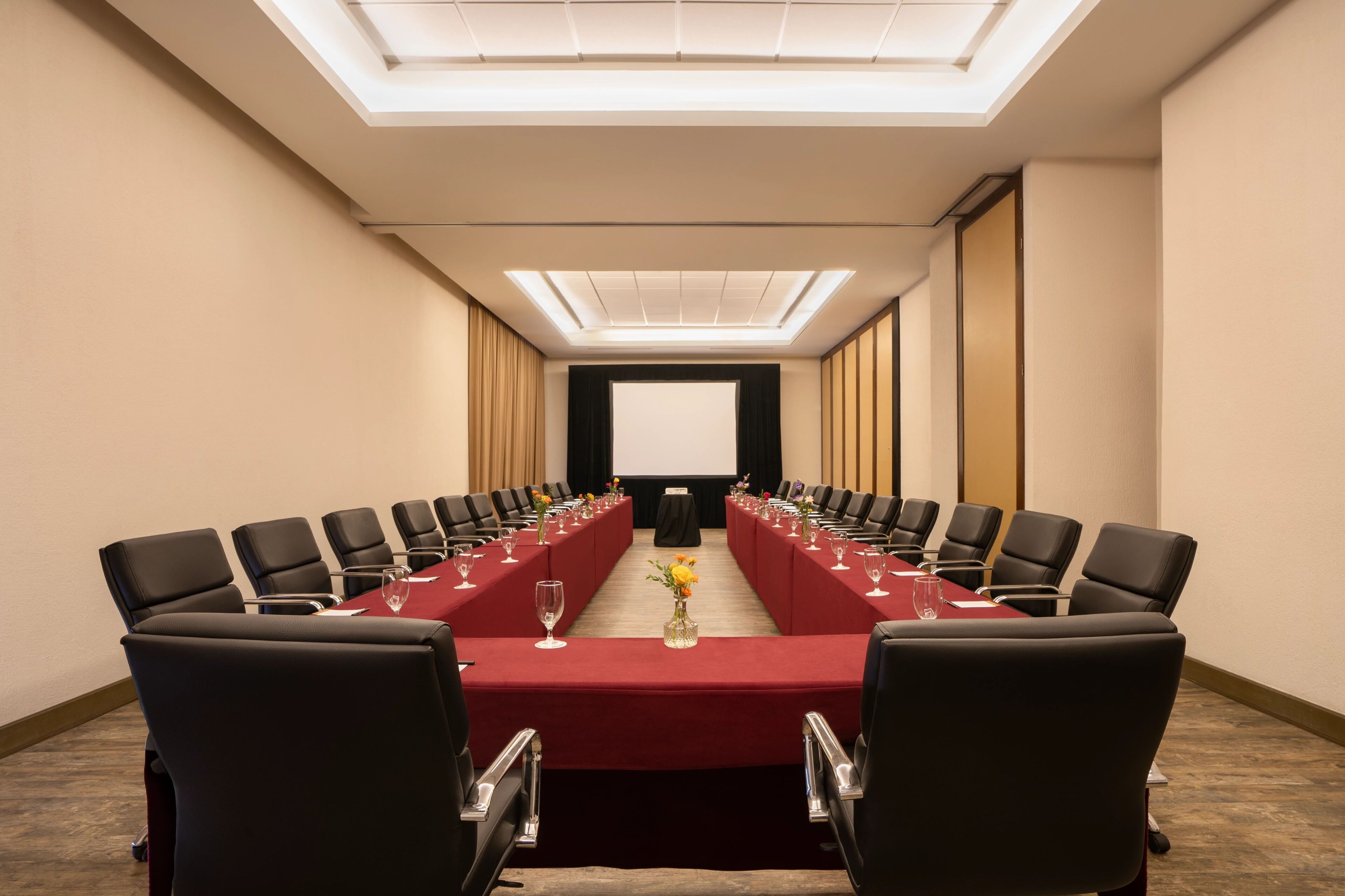A conference room with a long table, black chairs, and a projector screen at the front.
