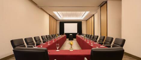 A conference room with a long table, black chairs, and a projector screen at the front.