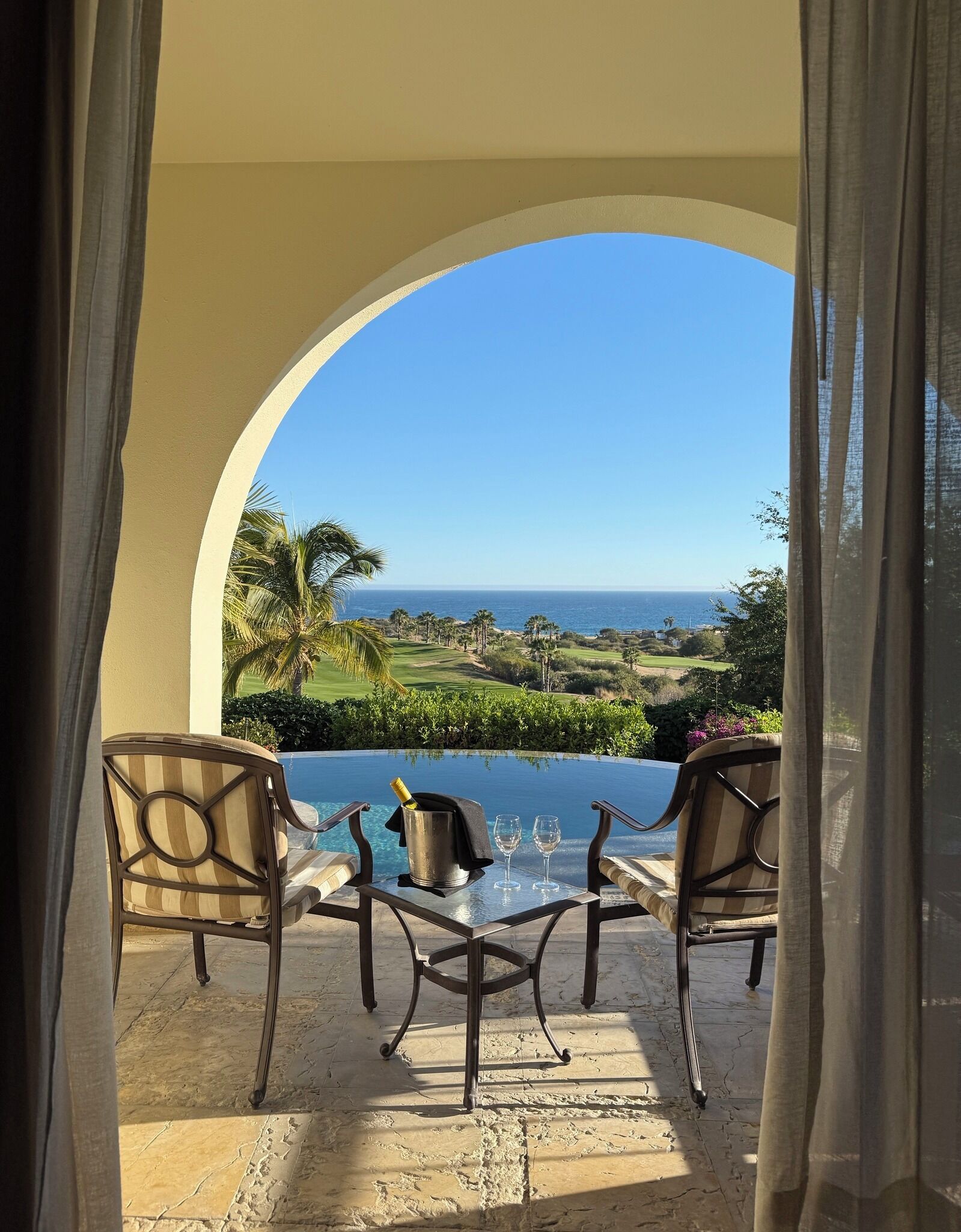 A patio with a table, two chairs, a champagne bottle, and two glasses.