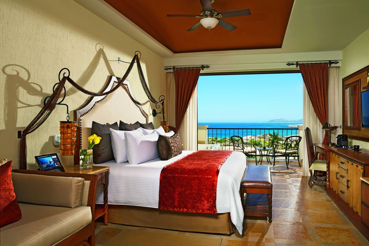 Quarto com cama, mesa de cabeceira e vista para o oceano.