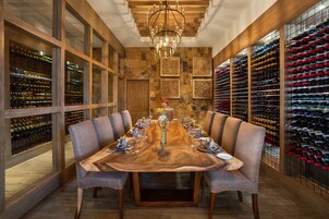 A formal dining room with a long wooden table, multiple wine racks, and a chandelier.