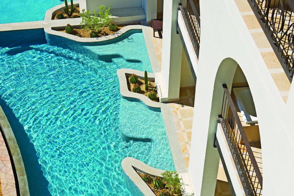 Piscina com uma pessoa na água, cercada por um edifício com varandas e áreas de estar ao ar livre.