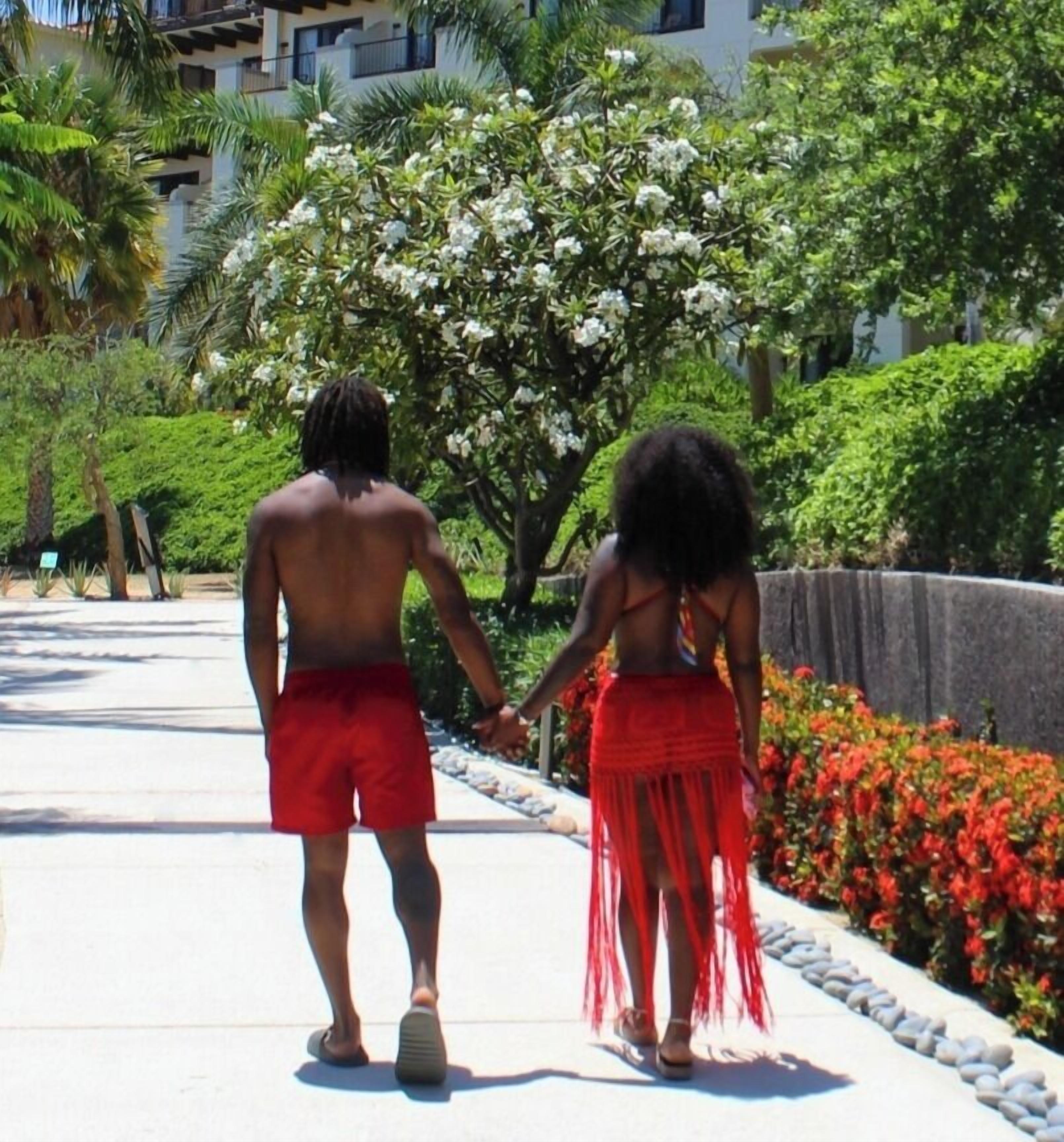 Two people walking on a pathway surrounded by greenery and flowers.