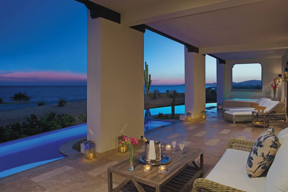 Uma área de estar ao ar livre luxuosa com vista para o mar, uma piscina e um pôr do sol.