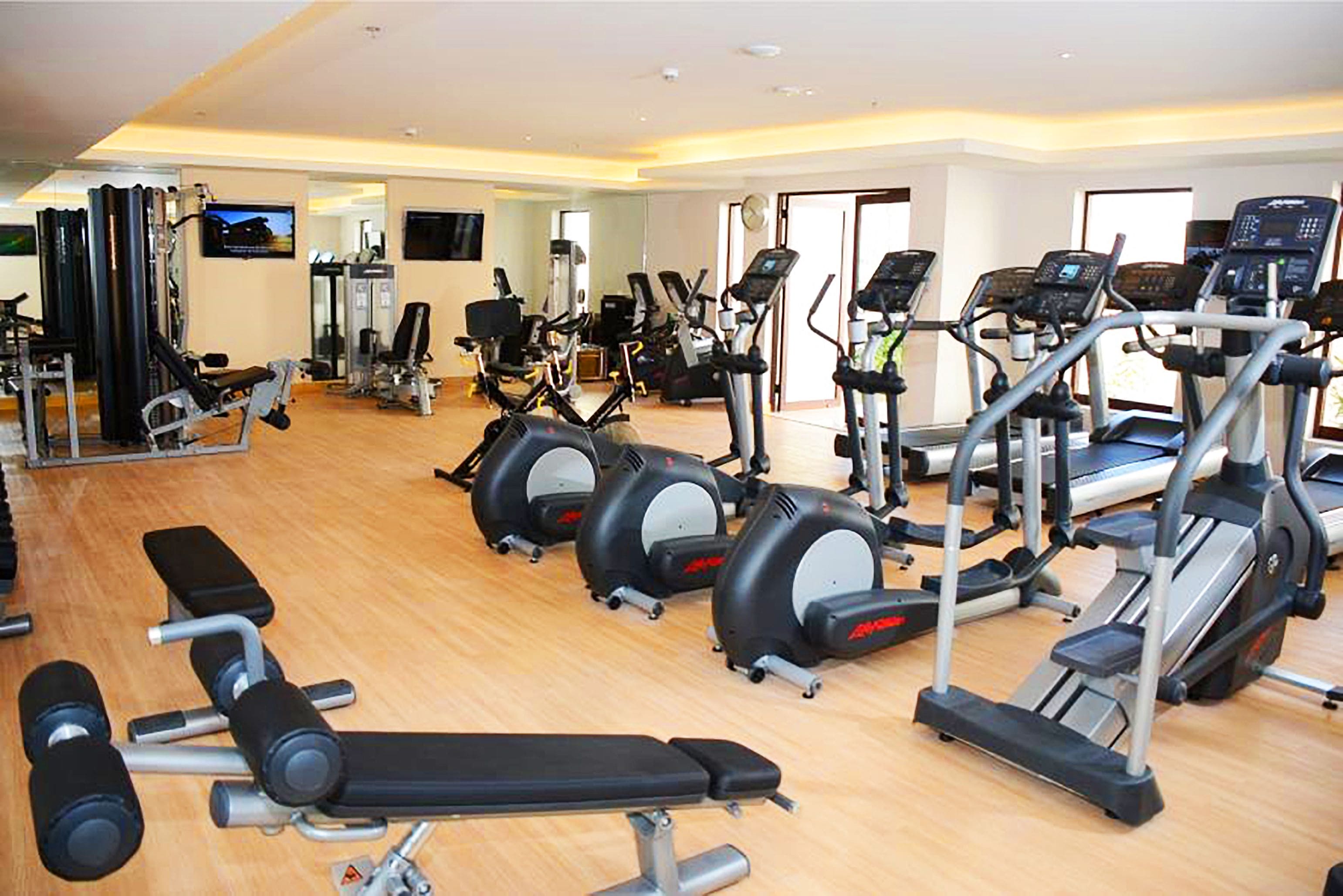 Un gimnasio con diverso equipo de ejercicio, incluyendo cintas de correr, elípticas y bancos de pesas.
