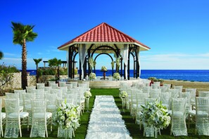 A beach wedding setup with a gazebo, white chairs, and a flower-lined aisle.