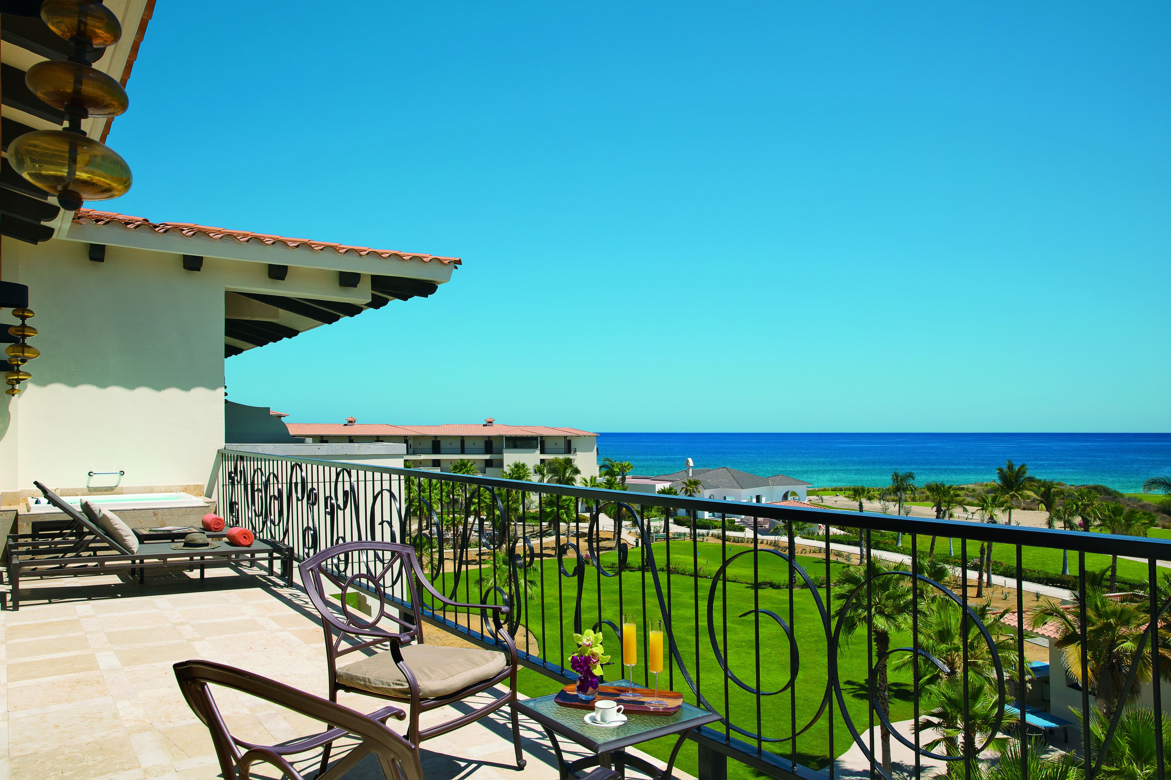 A balcony with a view of the ocean, lounge chairs, and a table with a drink.