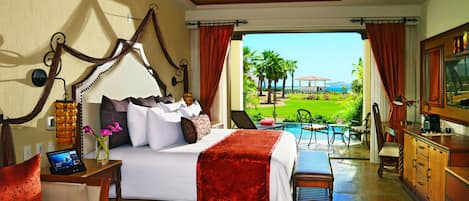Quarto de hotel com cama, escrivaninha, cadeira, televisão, janela com cortinas e vista para a piscina e jardim.