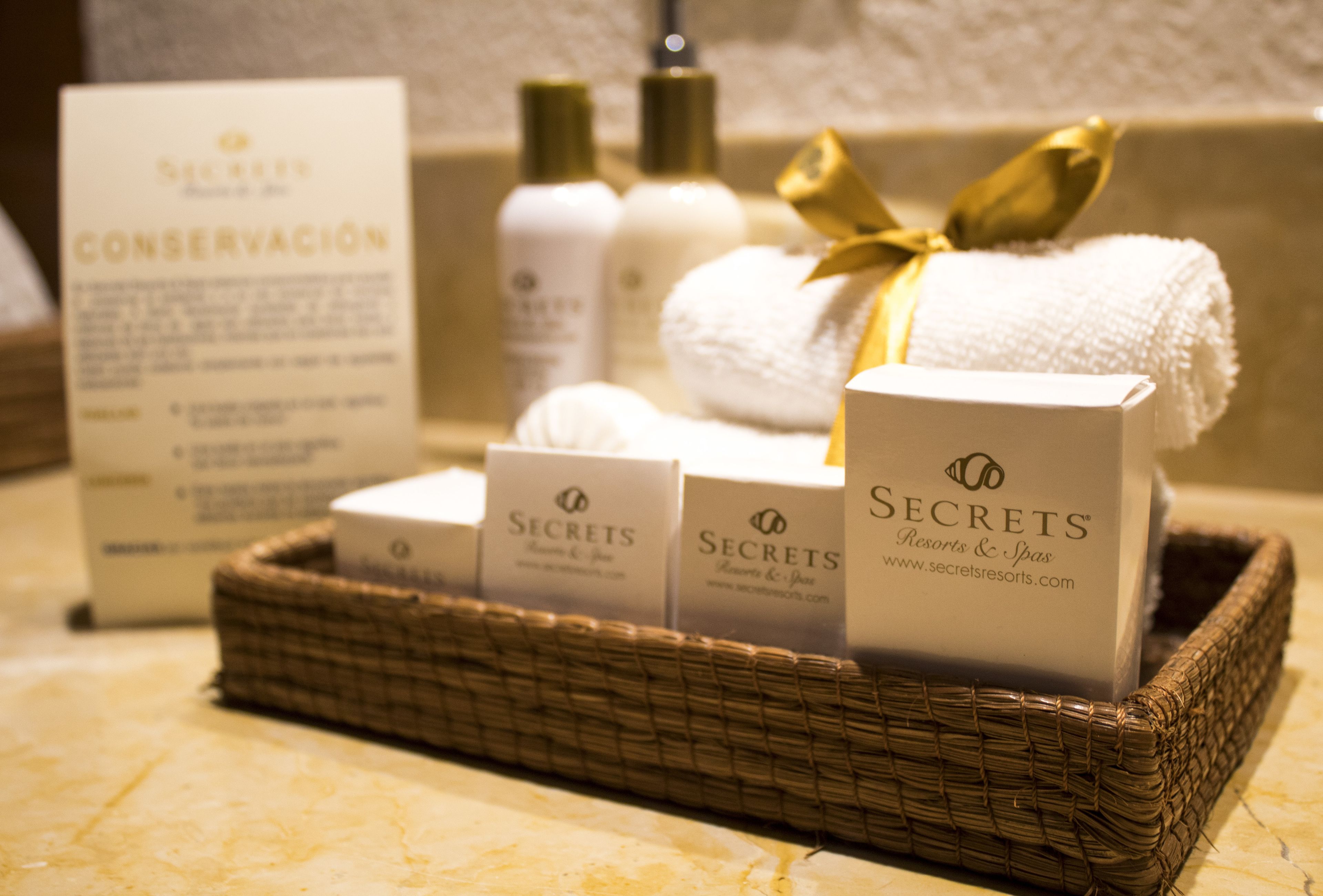 A wicker basket containing toiletries and a towel, with a sign and a bottle in the background.
