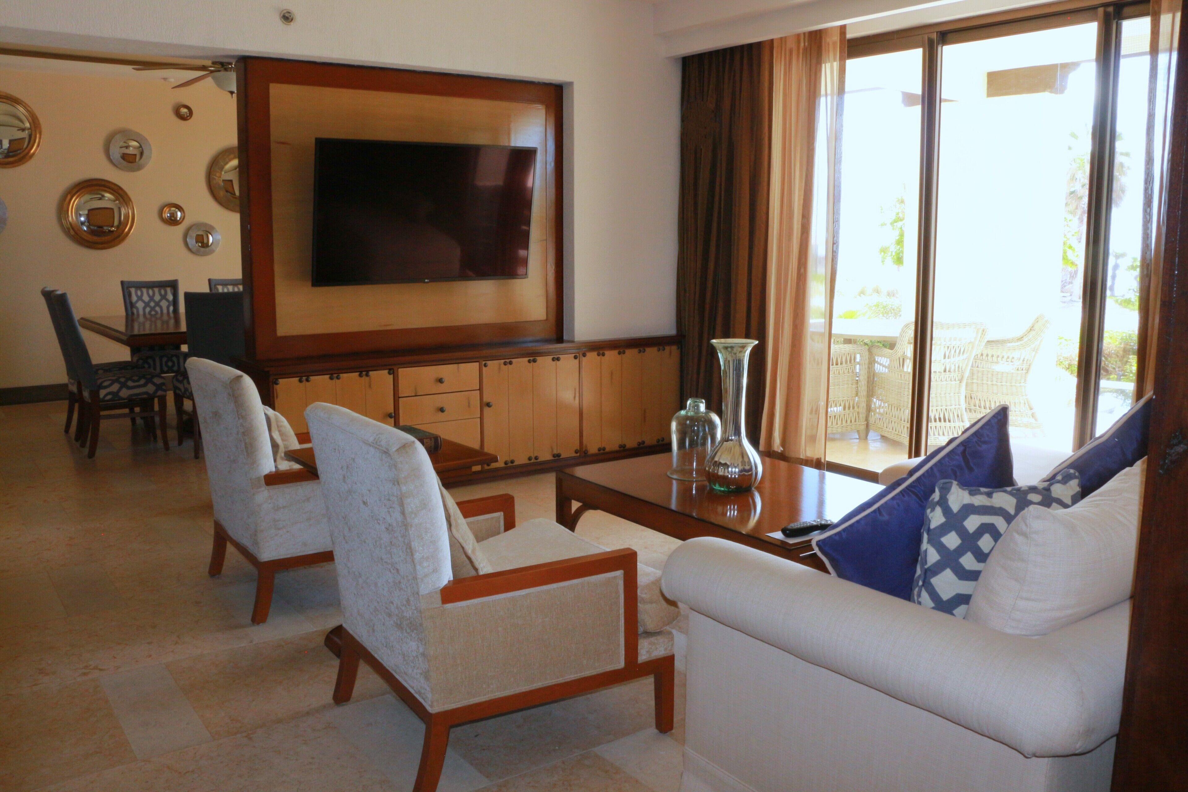 A living room with a flat-screen TV, two armchairs, a sofa, a coffee table, and a dining area with chairs and a table.