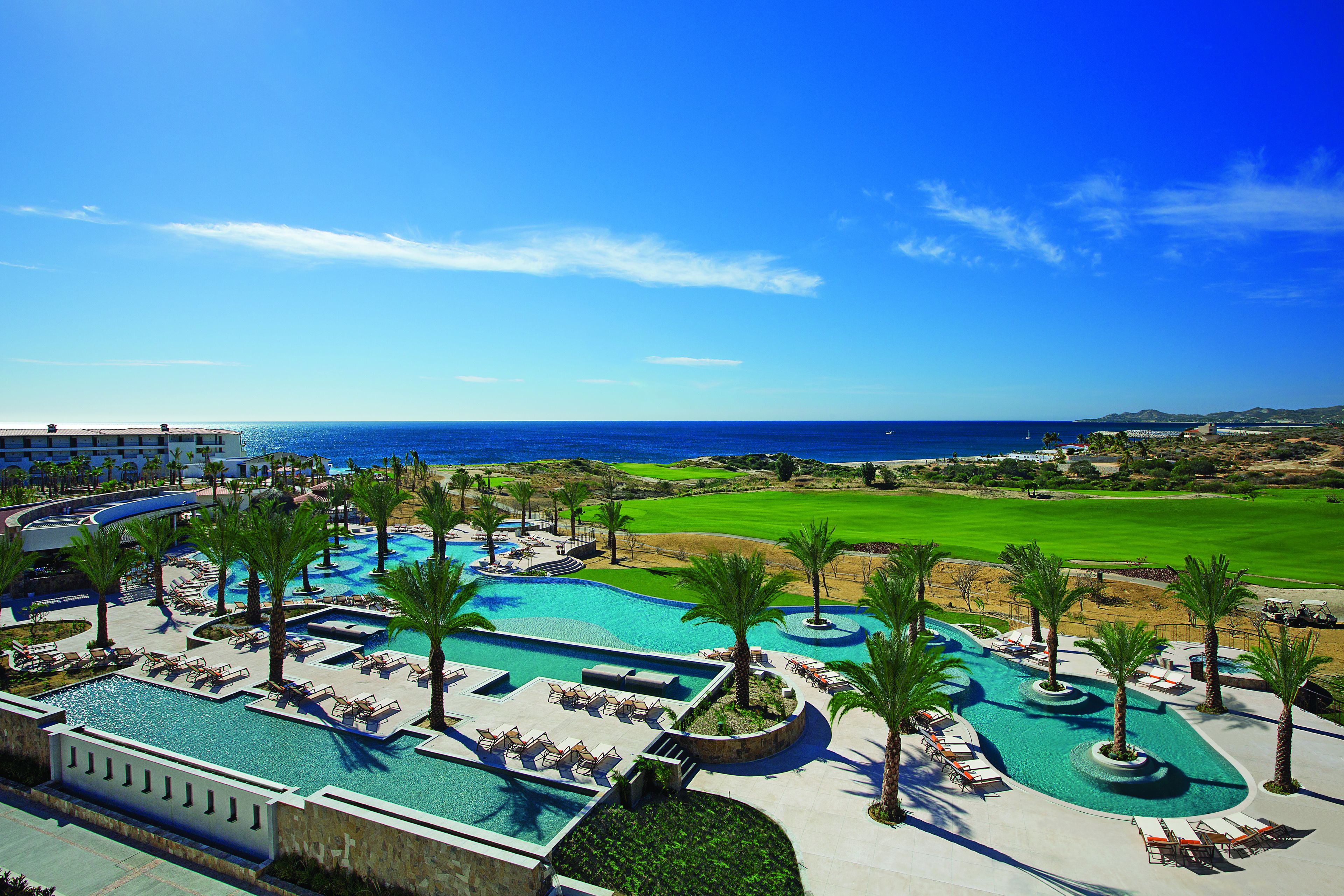 A resort with a large swimming pool, palm trees, and a view of the ocean.