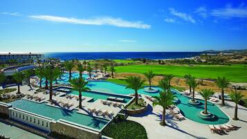 A resort with a large swimming pool, palm trees, and a view of the ocean.