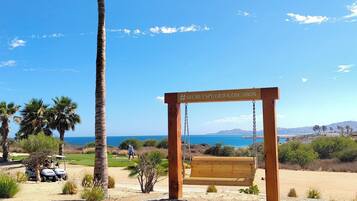 A wooden swing set with a bench, palm trees, and a clear blue sky.