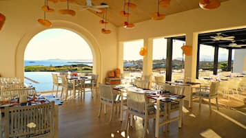 Comedor con mobiliario blanco, ventanas amplias y vista al mar.