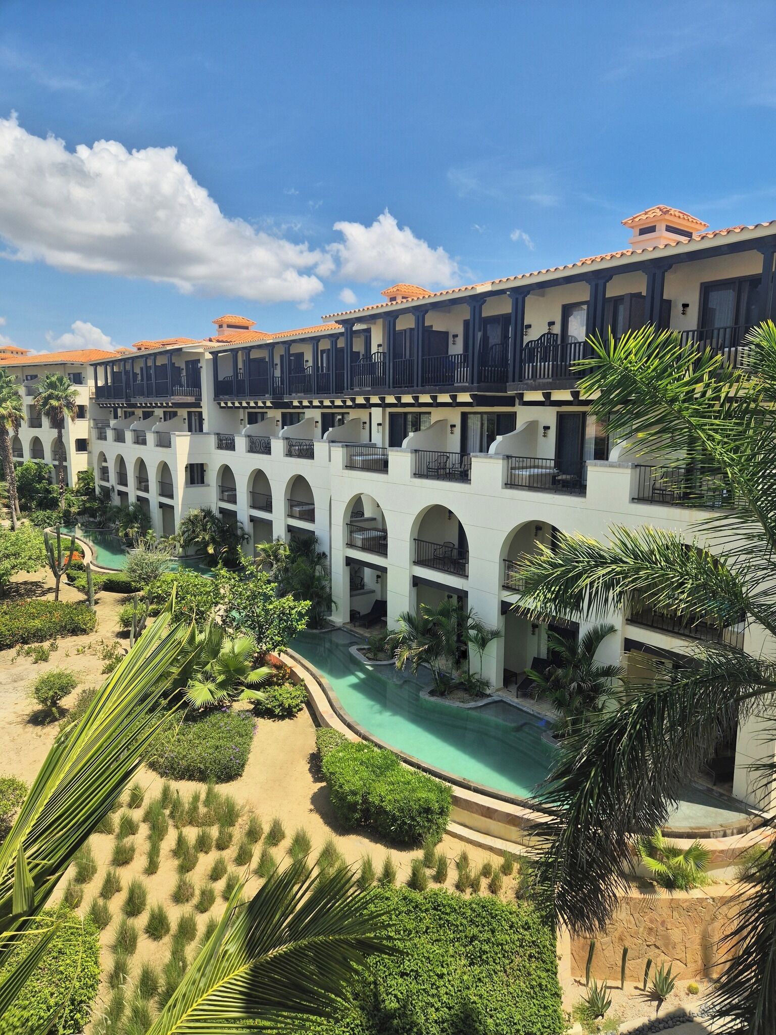 A hotel with multiple balconies, a swimming pool, and lush landscaping.