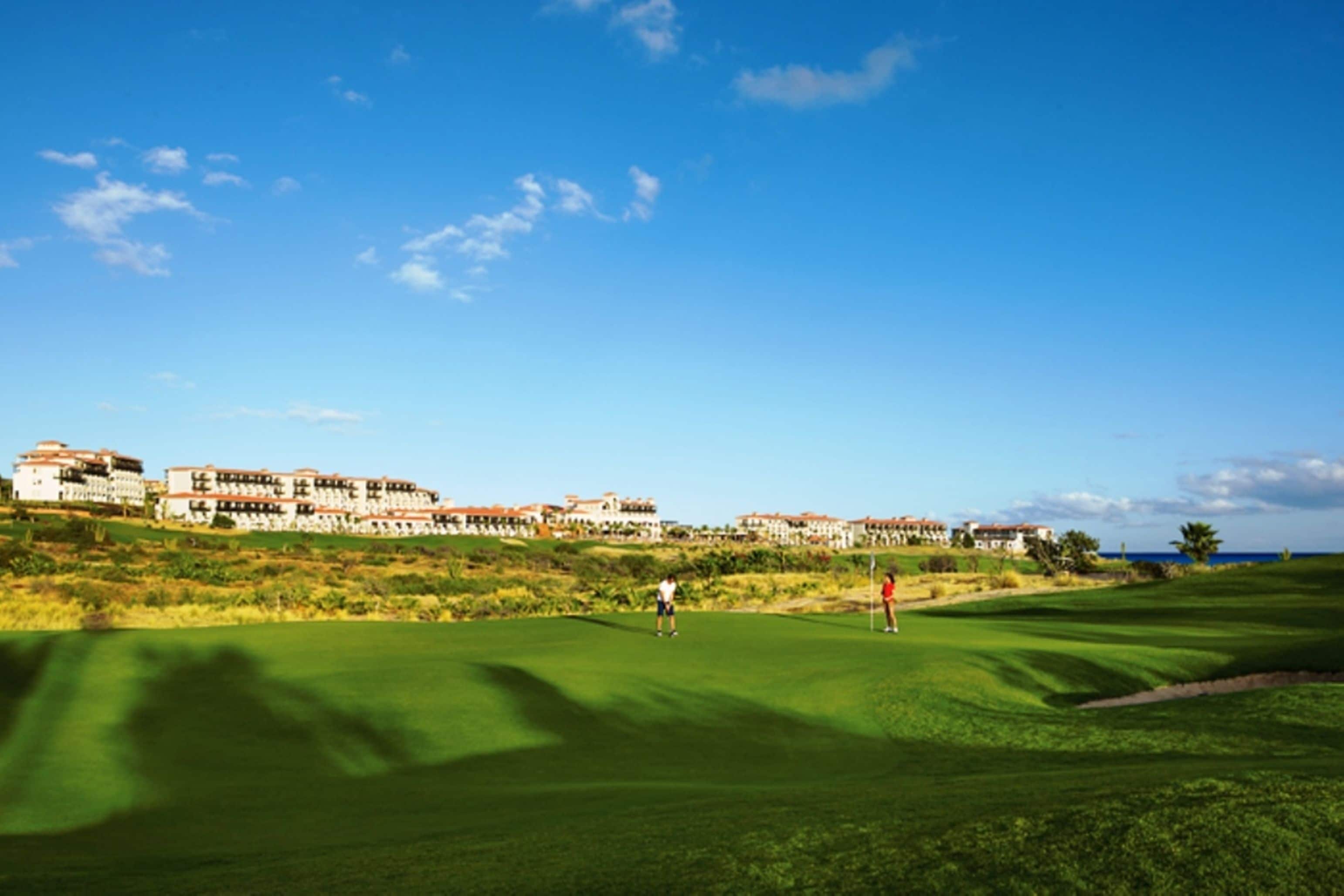 A golf course with a clear view of the ocean and a row of buildings in the background.