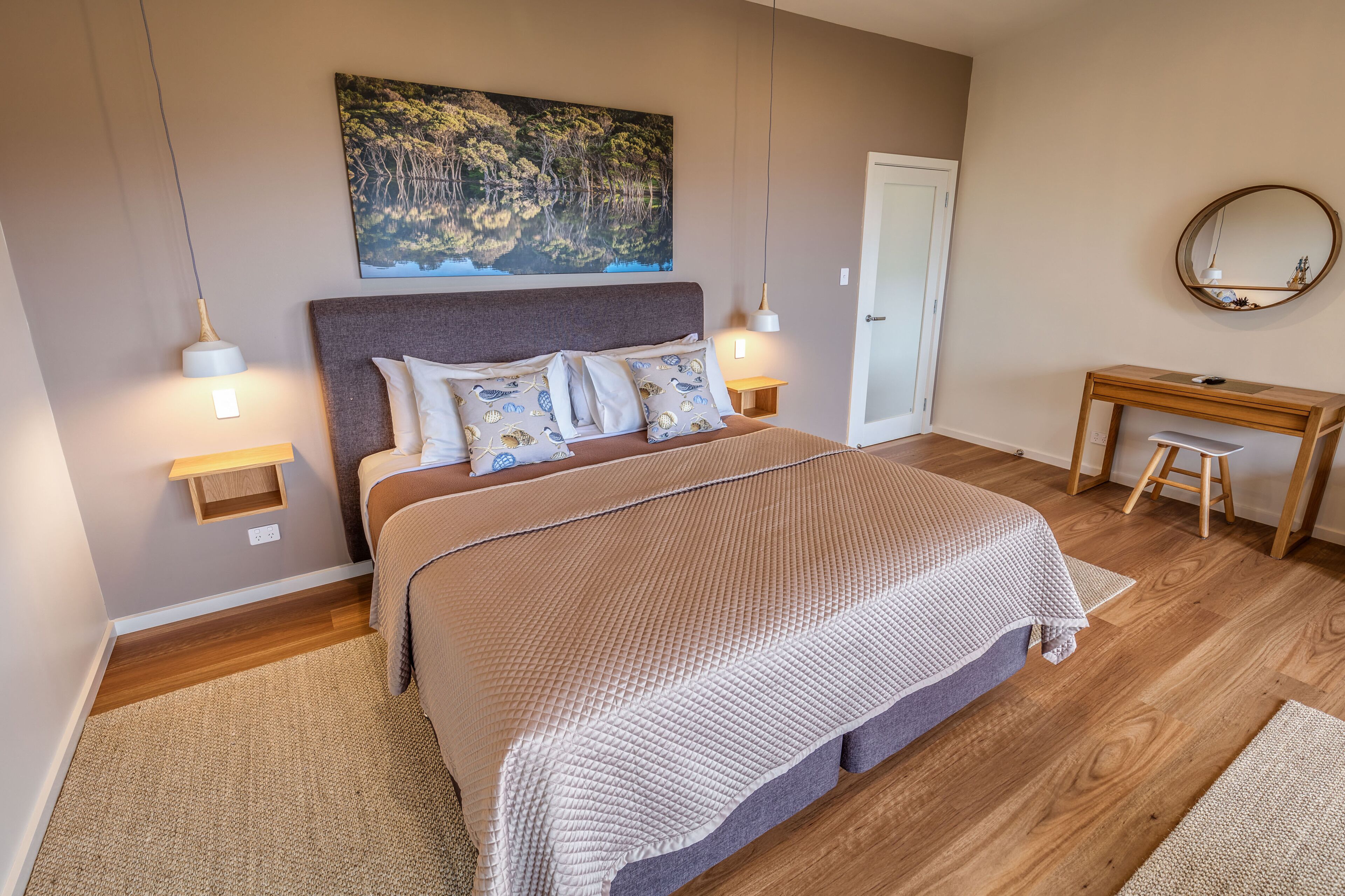 A bedroom with a large bed, bedside lamps, a desk, and a mirror.