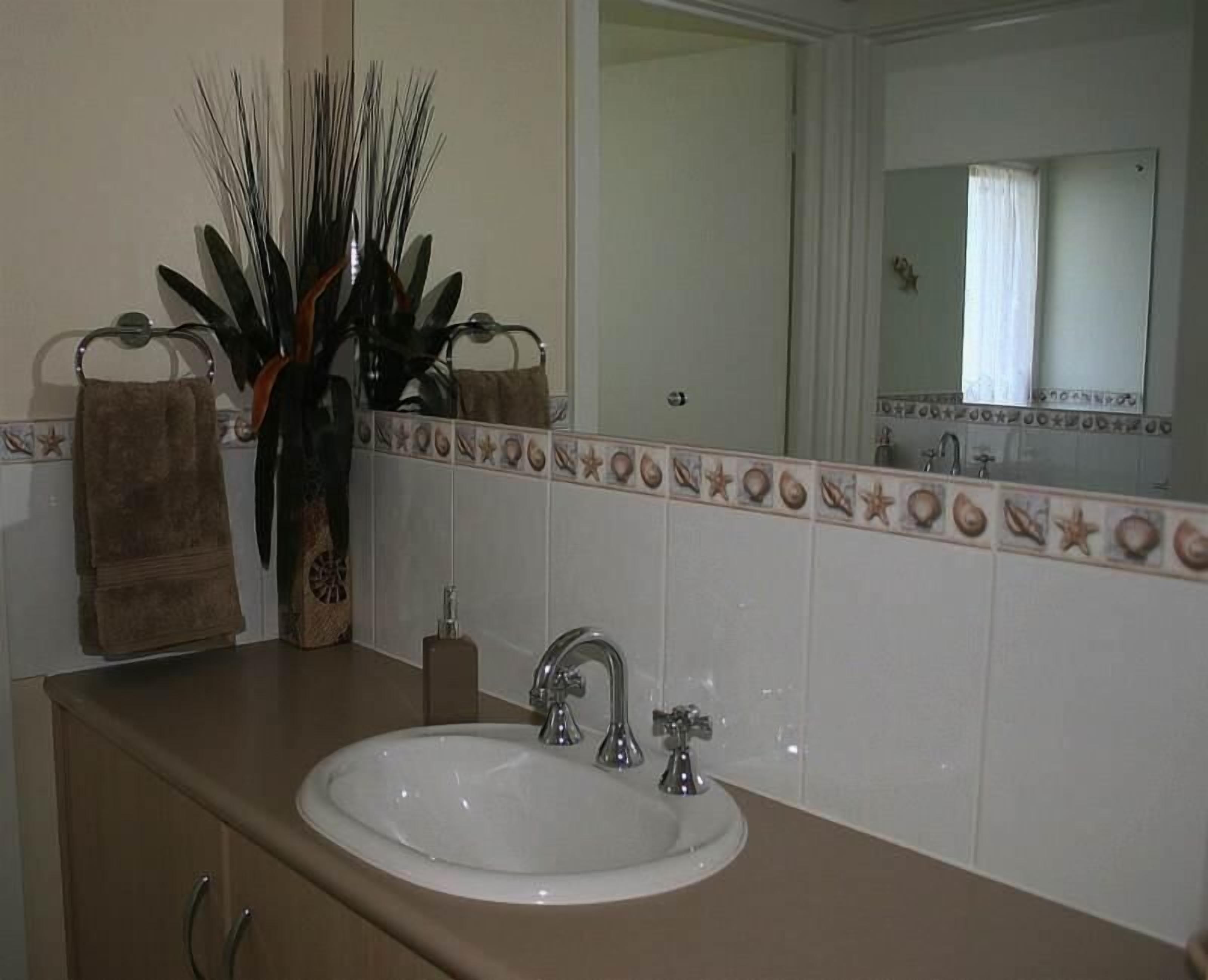 A bathroom with a white sink, two faucets, a mirror, and a decorative tile border.