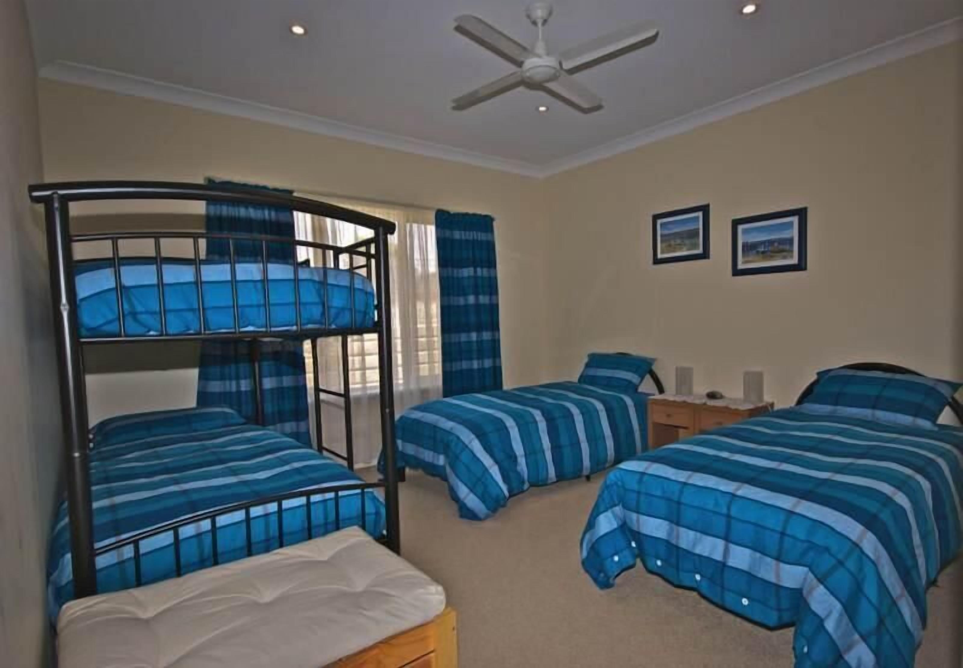 A bedroom with bunk beds, a ceiling fan, and two framed pictures on the wall.