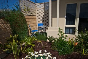 A small patio with a table and chairs, surrounded by a variety of plants and flowers. - Searenity Holiday Accommodation (Emu Bay)