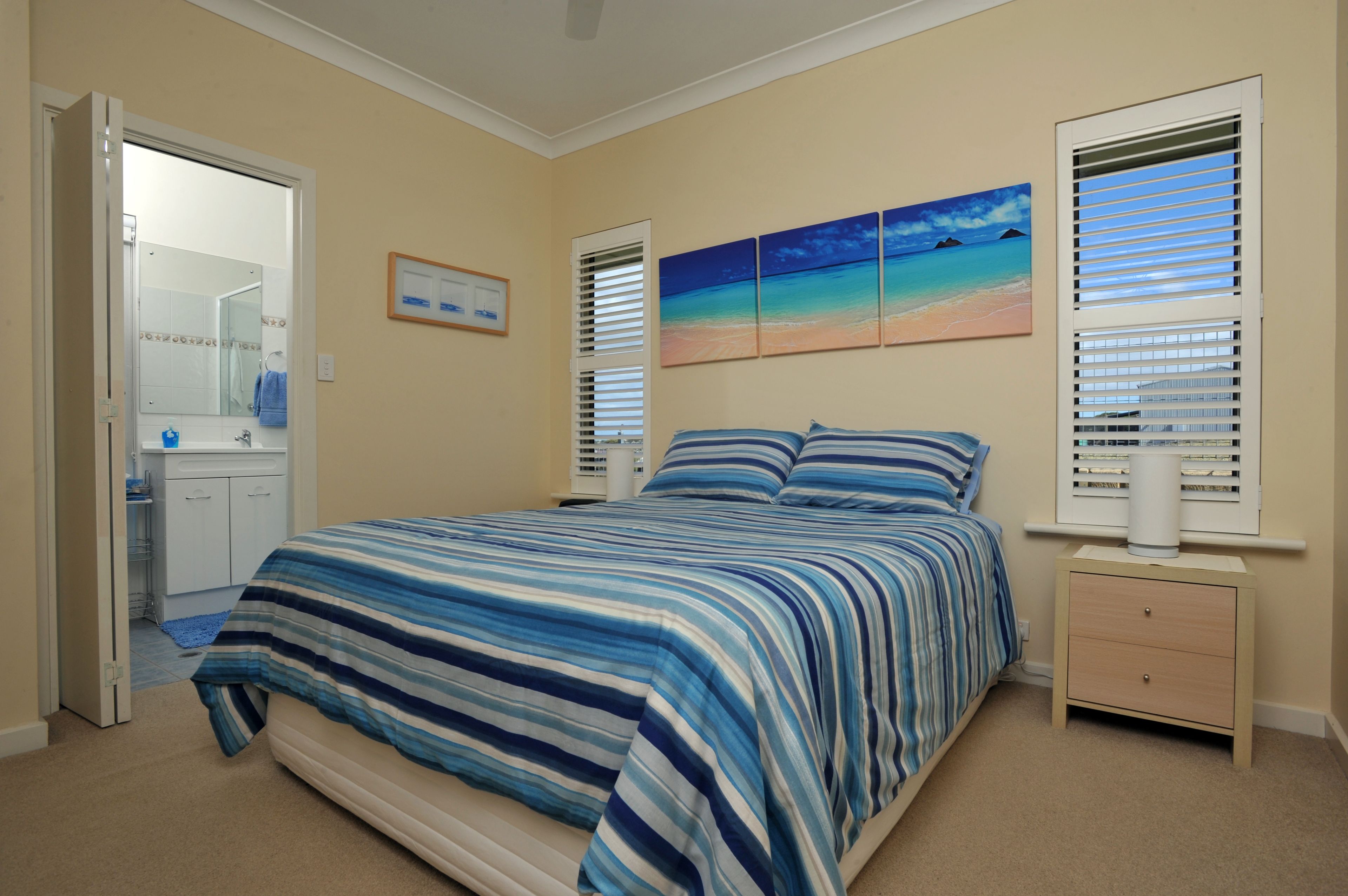 Un dormitorio con una cama, una mesita de noche, una ventana con persianas y un cuadro en la pared.