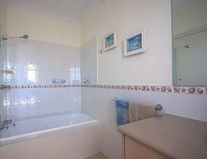 A bathroom with a bathtub, a sink, and a mirror. There are two framed pictures on the wall. - Searenity Holiday Accommodation (Emu Bay)