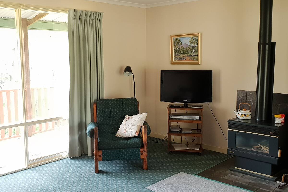A living room with a green armchair, a television on a wooden stand, a fireplace, and a painting on the wall.